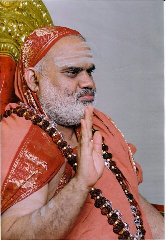 Jagadguru Sri Bharati Tirtha Mahaswamiji in profile, seated, raising his right hand in blessing, a saffron cloth draped over his head and rudraksha malas around his neck