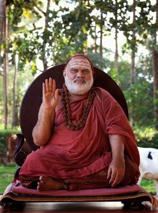 Jagadguru Sri Bharati Tirtha Mahaswamiji seated on a cushioned seat in a garden among trees, raising his right hand in blessing