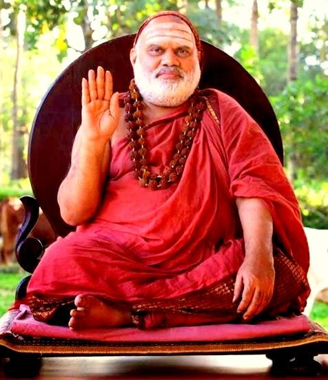 Jagadguru Sri Bharati Tirtha Mahaswamiji in red robes seated cross-legged on a throne in a garden, palm raised in blessing