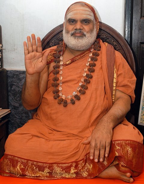Jagadguru Sri Bharati Tirtha Mahaswamiji in saffron robes seated on a dark carved seat, raising his right hand in blessing
